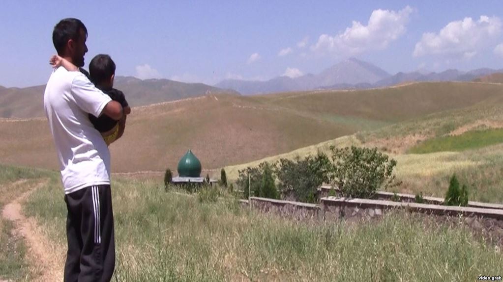 Житель Таджикистана с ребенком на руках стоит недалеко от места массового захоронения погибших во время гражданской войны. На этом кладбище похоронен отец этого мужчины.